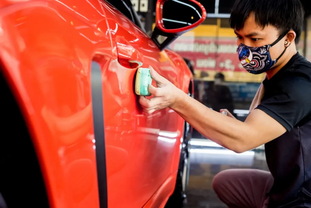 Car service technician carefully applying nano ceramic coating to a vehicle, enhancing paint protection and shine with durable ceramic car coating technology.